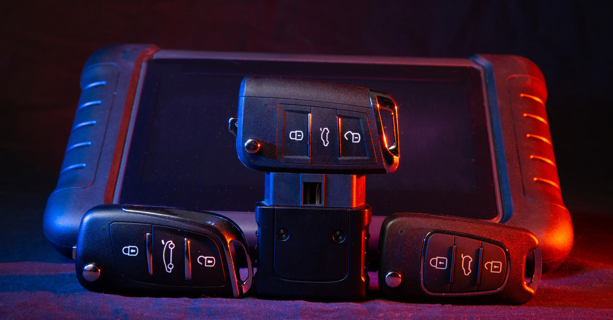 Closeup of three car key fobs and a key programming device behind it with a tint of red and blue light shining on it.