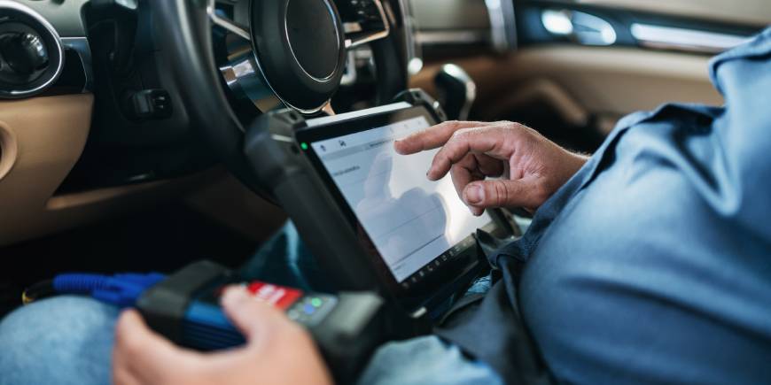 A technician in the driver's seat of a car using a diagnostic and programming device for car key programming.