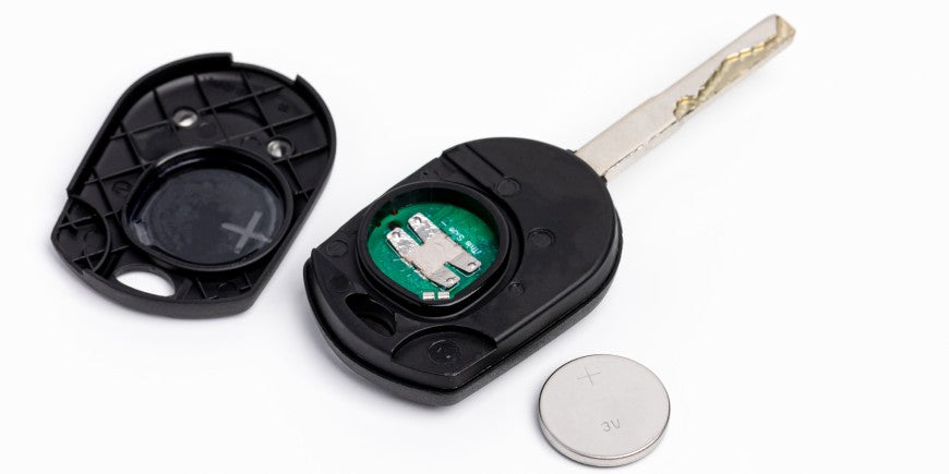 An opened key fob sits on a table with the plastic casing cover and a small battery on either side of it.