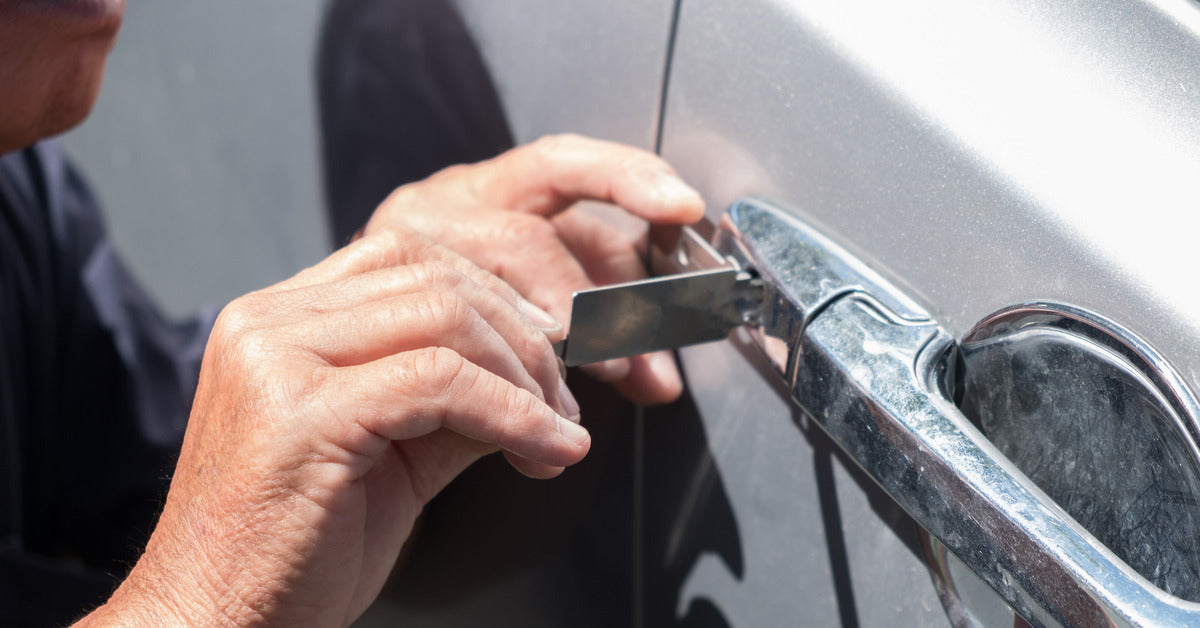 A man picking the lock of a car door with a professional lock pick. He is applying tension while manipulating the lock pick.