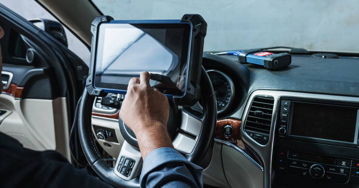 A man sitting in the driver's seat of a vehicle, using the touchscreen of a car key programming device.