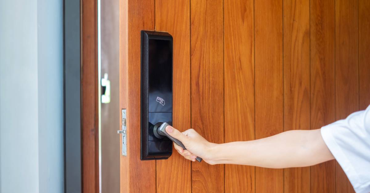 A person turning the handle of a wooden door. The handle is part of a digital smart lock security system.