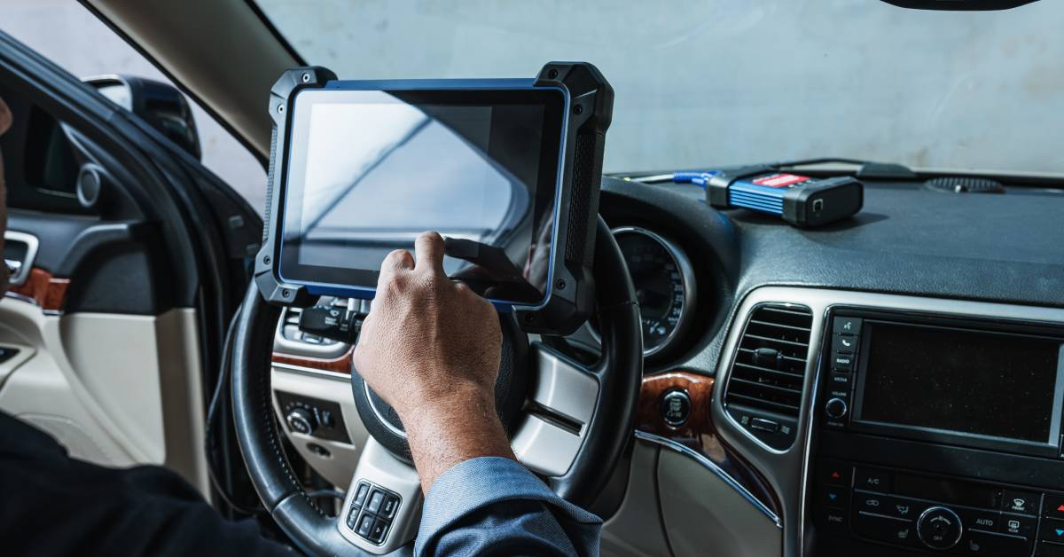 A locksmith sitting in the driver's seat of a car. He is working with a key programming and diagnostic device.