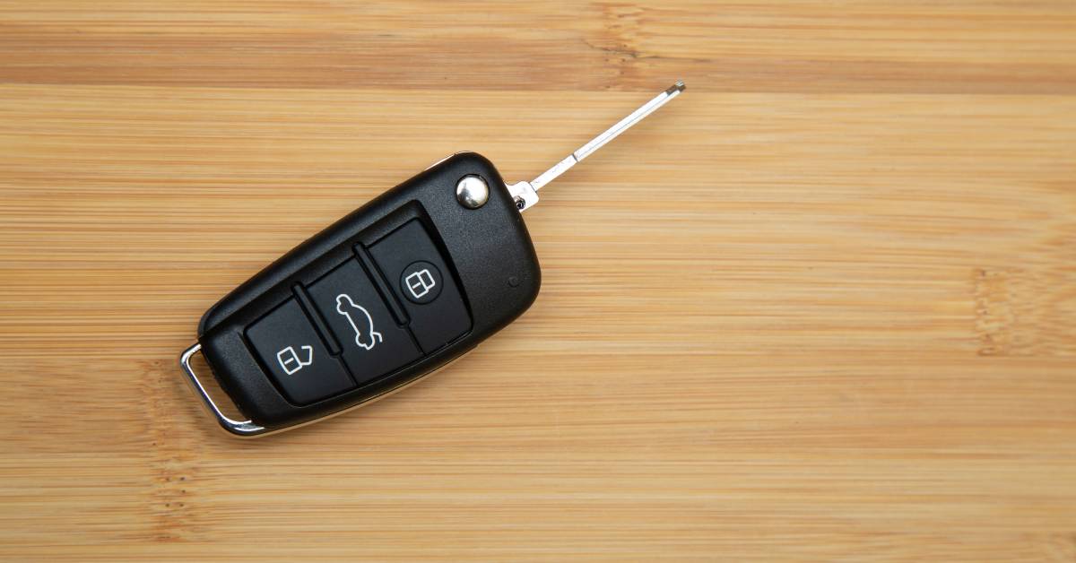 A modern car key with the key blade out. The fob has buttons for unlocking, locking, and opening the hatch of a car.